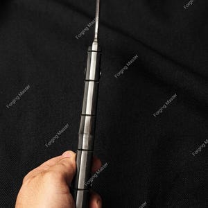 Puede incluir: Primer plano de un cuchillo con una hoja plateada y un mango negro y plateado. El mango tiene un dise&ntilde;o segmentado. El texto "Forging Master" se repite alrededor de la imagen.