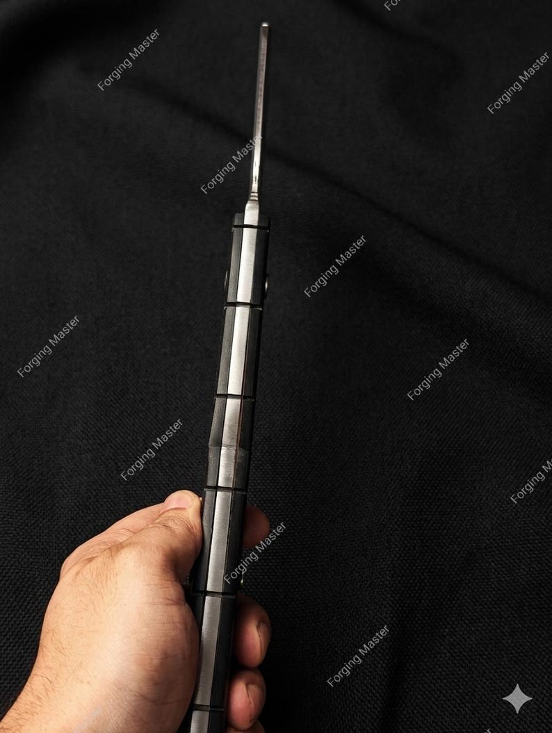 Puede incluir: Primer plano de un cuchillo con una hoja plateada y un mango negro y plateado. El mango tiene un dise&ntilde;o segmentado. El texto "Forging Master" se repite alrededor de la imagen.