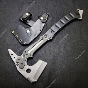 May include: A tactical axe with a black handle and a silver blade, accompanied by a black leather sheath. The axe features a textured grip and a sharp edge, designed for various outdoor and survival tasks.