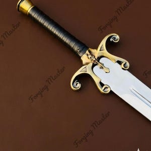 May include: A sword with a polished silver blade and a black wrapped handle. The hilt features a brass-colored crossguard with ornate, curved ends and a small skull emblem at the center. A brass-colored pommel caps the end of the handle.