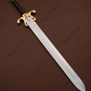 May include: A sword with a double-edged steel blade, a gold-colored metal crossguard featuring a central skull emblem, and a black wrapped handle with a gold-colored pommel. The blade has a central fuller, and the text Forging Master is visible.