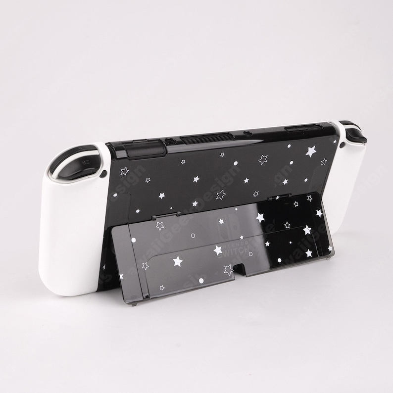 May include: Black and white Nintendo Switch console with a stand. The console is black with a white star pattern and white controllers. The stand is also black with a white star pattern. The console is designed to be used with the stand.