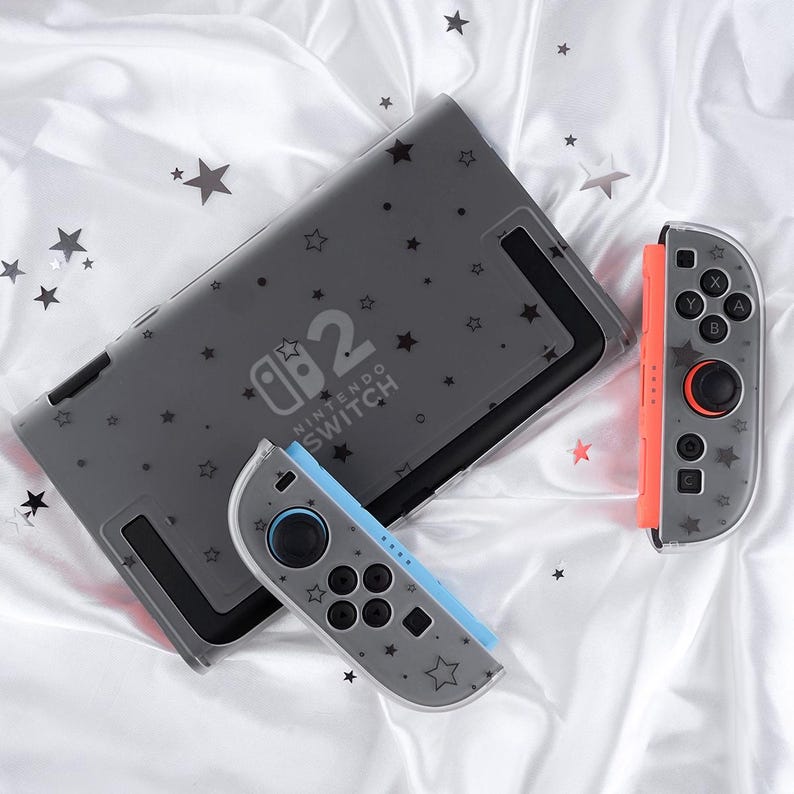 May include: A gray Nintendo Switch console and two controllers with a star pattern. The console has the text "Nintendo Switch 2". One controller is orange, the other is blue.