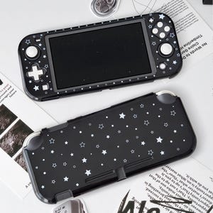 May include: A black handheld gaming console case featuring a white star and dot pattern. The set includes a front cover with cutouts for buttons and a screen, and a solid back cover, both decorated with a consistent celestial-themed graphic design.