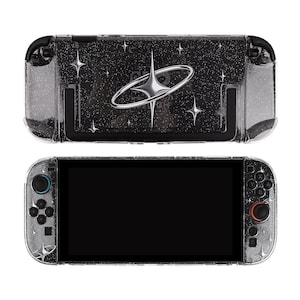 May include: A clear, glittery protective case for a game console. The case features a black background with a silver design of a ringed planet and starbursts. The game console has black controls and a black screen.