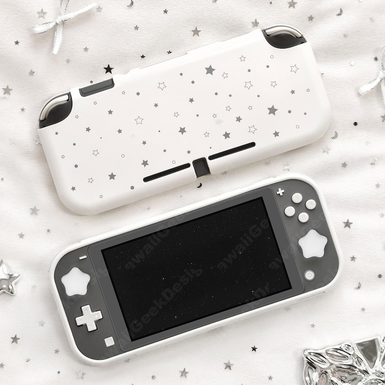 May include: A white Nintendo Switch Lite console and matching case. The case and console have a white background with a pattern of gray stars. The console has a black screen and gray accents. The text "GeekDesis" is visible on the screen.