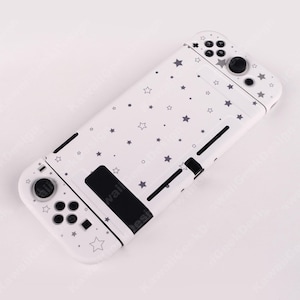 May include: White Nintendo Switch case with a pattern of gray stars and dots. The case has black buttons and control sticks. The design covers the entire case, including the buttons and the back.