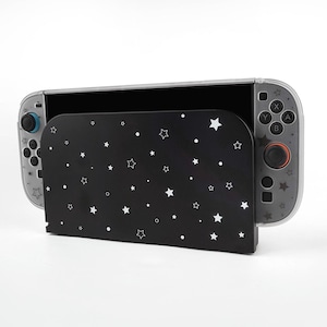 May include: A black protective case with a white star pattern is partially covering a clear and gray video game console. The console has blue and red control sticks and buttons. The case is designed to protect the console.