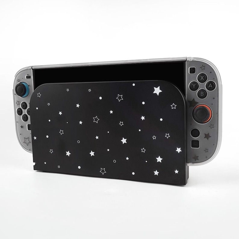 May include: A black protective case with a white star pattern is partially covering a clear and gray video game console. The console has blue and red control sticks and buttons. The case is designed to protect the console.