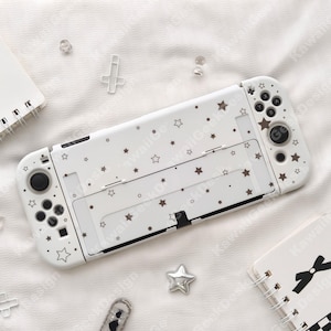 May include: White Nintendo Switch case decorated with brown stars and dots. The case has cutouts for buttons and ports. The design includes the text "Kawaii Design".