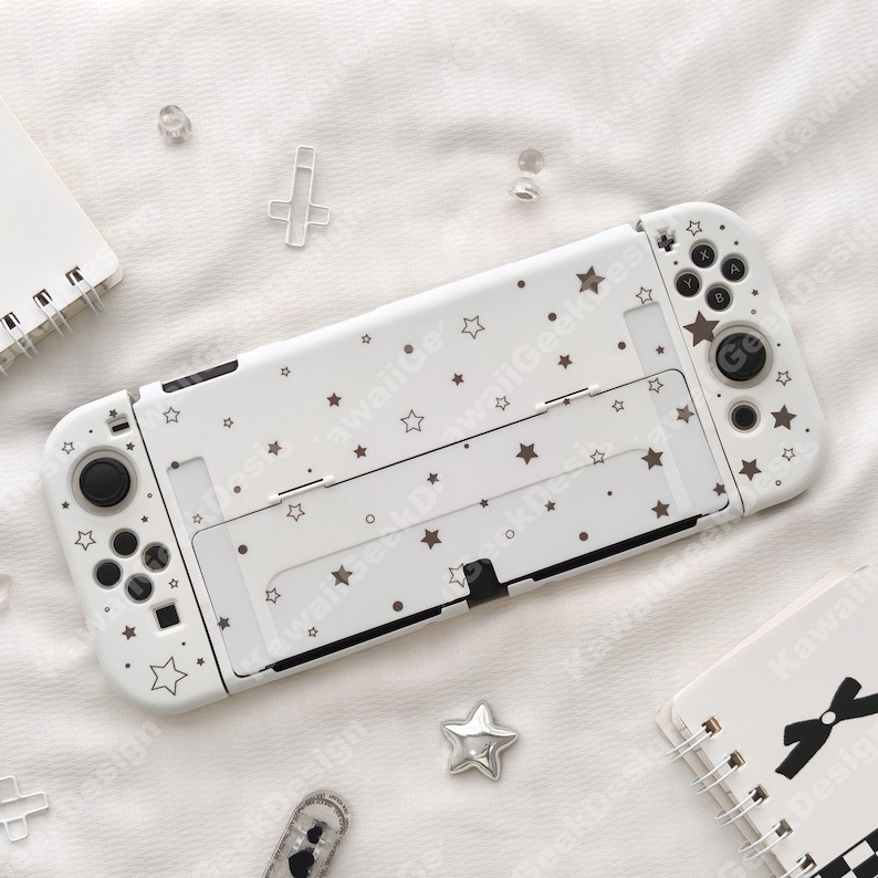 May include: White Nintendo Switch case decorated with brown stars and dots. The case has cutouts for buttons and ports. The design includes the text "Kawaii Design".