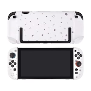 May include: White gaming console with a black screen and a white back with a gray star pattern. The console has black accents and buttons with a red joystick. The top part of the console is also white with a gray star pattern.