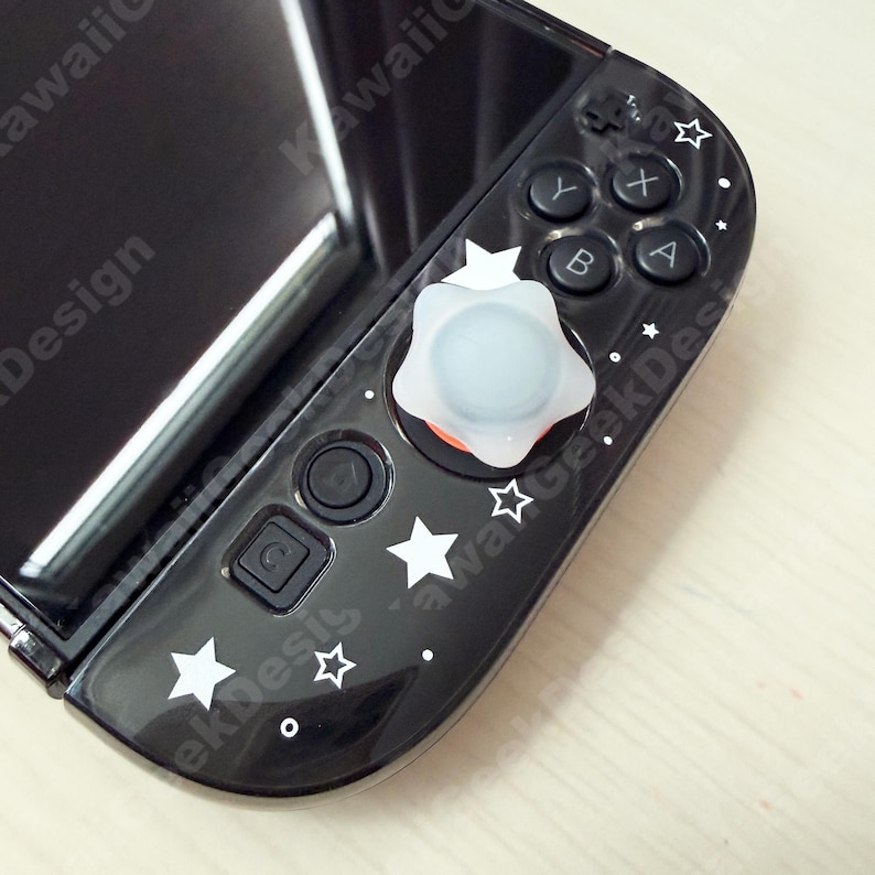 May include: Black Nintendo Switch Joy-Con controller with white star and dot decals. A white and light blue star-shaped thumb grip is on the joystick. The controller has black buttons with white lettering.