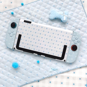 May include: A handheld gaming console featuring a light blue skin with a white snowflake and dot pattern. The device includes black joysticks, one with a blue accent and one with a red accent, and light blue buttons with white symbols.