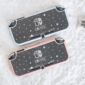 May include: Two Nintendo Switch Lite handheld gaming consoles, one in light blue and one in light pink, featuring a dark gray back panel decorated with white star patterns and the Nintendo Switch logo printed in the center of each device.