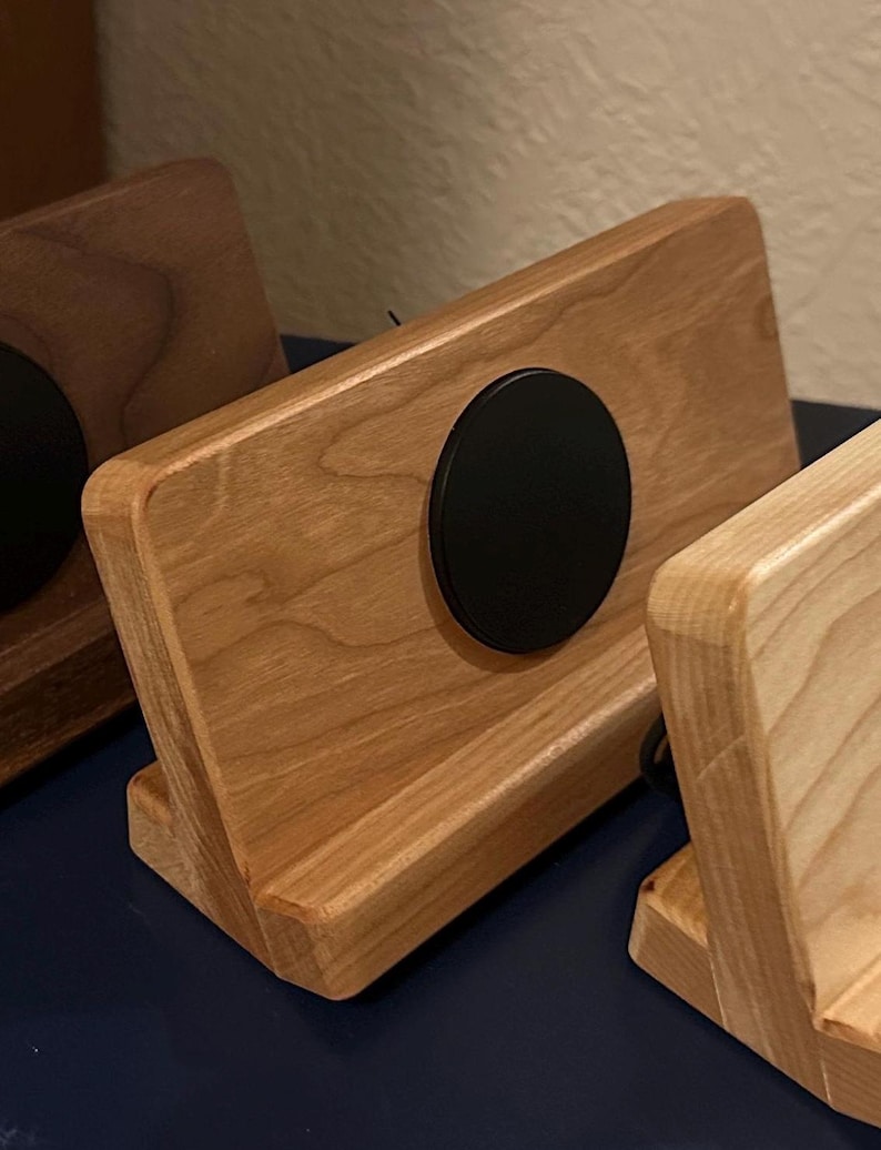 Puede incluir: Soporte de tel&eacute;fono de madera con acabado natural y un acento circular negro. El soporte est&aacute; inclinado para una visualizaci&oacute;n &oacute;ptima y tiene una ranura para sostener un tel&eacute;fono o tableta. La veta de la madera es visible.