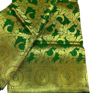 May include: Green fabric with gold floral and paisley patterns. The fabric has a gold border with circular and geometric designs. The fabric is folded and draped, showcasing the intricate details of the design. The fabric is likely used for clothing or home decor.