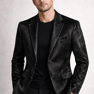 May include: A black blazer with a textured pattern, paired with a black t-shirt and trousers. The blazer has a classic two-button closure and a notched lapel. The outfit is a monochromatic ensemble.
