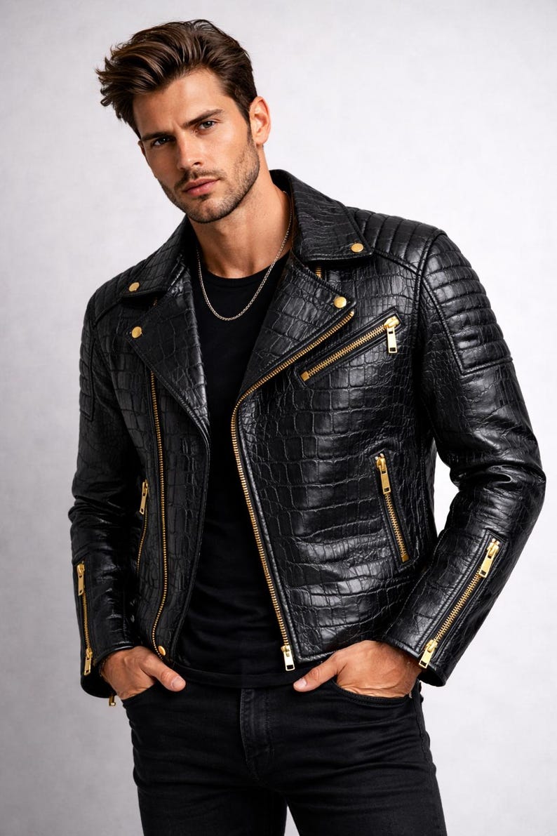 May include: Black leather jacket with a crocodile skin texture, featuring gold zippers and hardware. The jacket has a classic biker style with a notched collar and quilted shoulder details. The model is wearing a black shirt and black jeans.