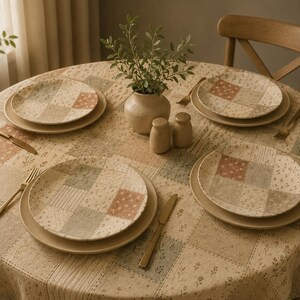 May include: A round dining table set with four place settings, each featuring a patterned plate on a solid plate, a gold-toned knife and fork, a central beige vase with green foliage, and two small beige shakers on a patchwork tablecloth.