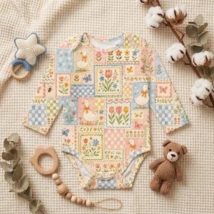 Puede incluir: Un body de beb&eacute; de manga larga con un dise&ntilde;o de patchwork con patos, flores y mariposas en colores pastel. Tambi&eacute;n se ven un sonajero en forma de estrella, un mordedor de madera y un peque&ntilde;o osito de peluche.