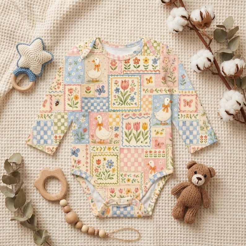 Puede incluir: Un body de beb&eacute; de manga larga con un dise&ntilde;o de patchwork con patos, flores y mariposas en colores pastel. Tambi&eacute;n se ven un sonajero en forma de estrella, un mordedor de madera y un peque&ntilde;o osito de peluche.