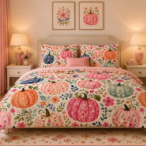 May include: A bedding set featuring a cream-colored base with a repeating pattern of pumpkins in shades of orange, pink, blue, and green, interspersed with small floral motifs and green leaves. The set includes a comforter and two matching pillow shams.