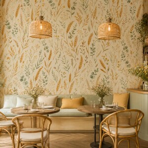 K&ouml;nnte beinhalten: Ein Caf&eacute;-Innenraum mit einer Tapete mit botanischem Muster aus Weizenhalmen und gr&uuml;nen Bl&auml;ttern. Zwei runde Holztische sind mit Rattanst&uuml;hlen und einer langen hellgr&uuml;nen Sitzbank mit gelben und wei&szlig;en Kissen unter Korblampen kombiniert.