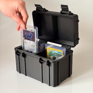 Peut inclure: Un boîtier de rangement rigide, rectangulaire et noir, doté d'un couvercle à charnière et de deux compartiments internes. Le boîtier contient plusieurs cartes à collectionner sous pochettes transparentes, dont une Umbreon et une Feraligatr.