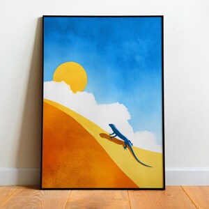 May include: Framed art print depicting a desert scene with a blue lizard on a sand dune. The artwork features a blue sky, a yellow sun, and white clouds. The dune is orange and yellow.
