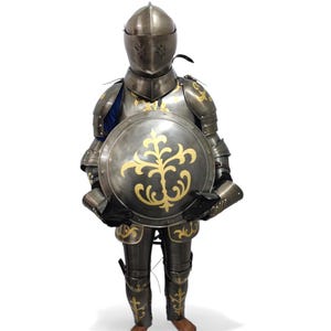 Peut inclure: Une armure médiévale complète en argent et or. L'armure comprend un casque, une cuirasse, des protège-bras et de jambes, et un bouclier rond. Le bouclier présente un motif floral doré. L'armure est conçue pour être portée.