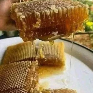 May include: A close-up of a honeycomb dripping with golden honey. The honeycomb is a rich amber color, with a complex, geometric pattern. Several pieces of honeycomb are on a white plate, with honey dripping down.
