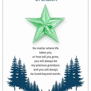 May include: A white greeting card featuring a translucent light green star at the center. The text reads TO MY Grandson followed by a poem about love. Dark blue silhouettes of birds fly at the top, and dark blue pine trees frame the bottom.