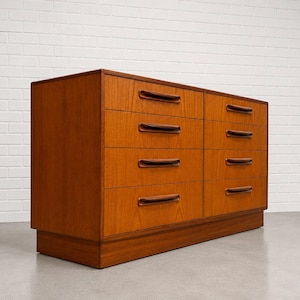 May include: A mid-century modern dresser with six drawers. The dresser is made of wood with a warm, reddish-brown finish. Each drawer has a dark brown, curved handle. The dresser sits on a low, rectangular base.