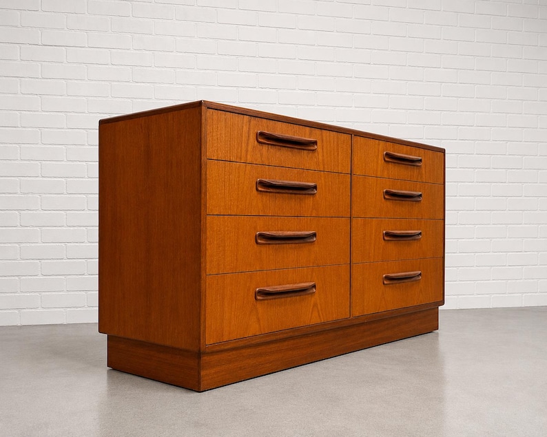 May include: A mid-century modern dresser with six drawers. The dresser is made of wood with a warm, reddish-brown finish. Each drawer has a dark brown, curved handle. The dresser sits on a low, rectangular base.