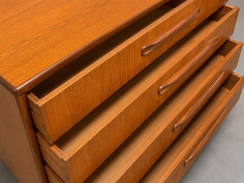 May include: A wooden dresser with four open drawers. The dresser is made of light brown wood with a smooth finish. Each drawer has a curved handle. The drawers are partially pulled out, revealing the interior.