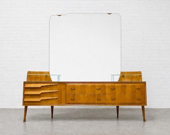 Könnte beinhalten: Eine Kommode aus Holz im Mid-Century-Stil mit einem großen rechteckigen Spiegel. Die Kommode hat mehrere Schubladen und ein einzigartiges Design mit hellbraunem Finish und konischen Beinen. Der Spiegel ist von einer dünnen Metallverkleidung umrahmt.