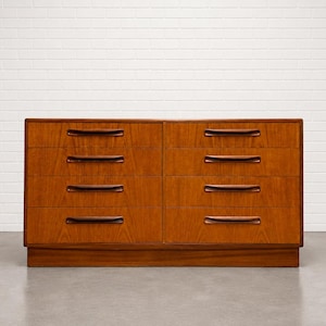 May include: A mid-century modern dresser with six drawers. The dresser is made of wood with a warm, reddish-brown finish. Each drawer has a dark brown, curved handle. The dresser is set against a white brick wall.