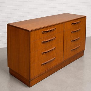 May include: A mid-century modern wooden dresser with eight drawers. The dresser is made of light brown wood and has a rectangular shape. The drawers have curved, recessed handles.