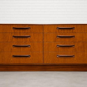 May include: A mid-century modern dresser with six drawers. The dresser is made of wood with a warm brown finish. Each drawer has a dark brown, curved handle. The dresser sits on a low, rectangular base.