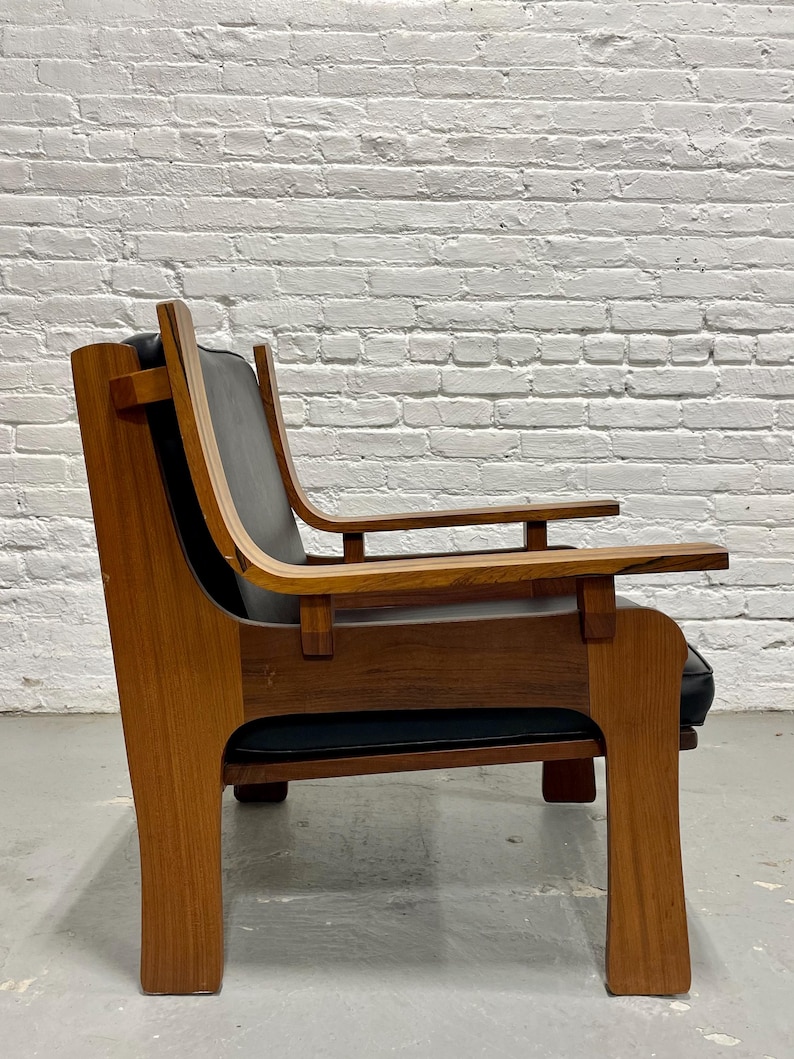 May include: A mid-century modern armchair with a wooden frame and black leather seat and back. The chair has a curved backrest and armrests, and a sturdy, geometric base. The wood has a warm, natural finish.