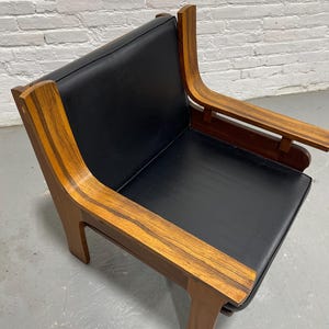 May include: A mid-century modern armchair with a black seat and backrest. The chair features curved wooden armrests and a wooden frame with a warm, natural finish. The design is minimalist and stylish, suitable for a living room or lounge area.