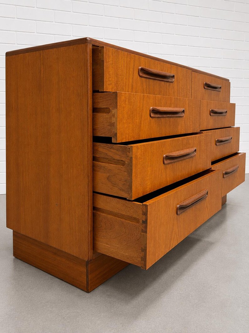 May include: A mid-century modern dresser with eight drawers, crafted from warm-toned wood. The drawers feature integrated, curved handles. Several drawers are open, revealing the dovetail joinery. The dresser sits on a low, rectangular base.