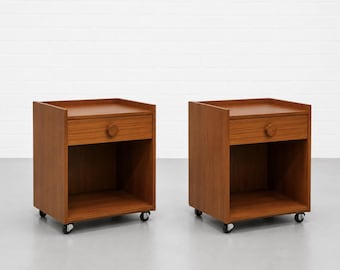 May include: Two matching wooden nightstands with a warm brown finish. Each nightstand has a drawer with a circular wooden knob and an open shelf below. They are on small wheels for easy movement.