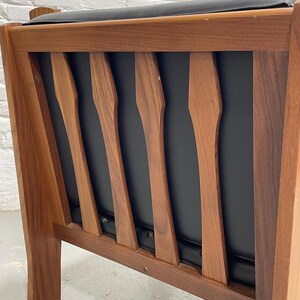 May include: Mid-century modern armchair with a wooden frame and black seat and back. The chair features a series of vertical wooden slats on the backrest, and the frame is made of a warm-toned wood. The seat and back appear to be upholstered.