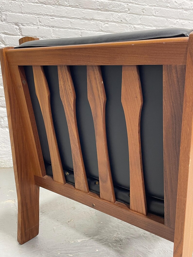 May include: Mid-century modern armchair with a wooden frame and black seat and back. The chair features a series of vertical wooden slats on the backrest, and the frame is made of a warm-toned wood. The seat and back appear to be upholstered.