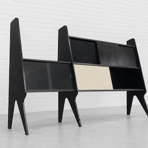 May include: A black wooden shelving unit with an asymmetrical, tiered design featuring three tall, angled side supports. The unit includes multiple storage compartments with sliding doors, including one light-colored panel in the center section.