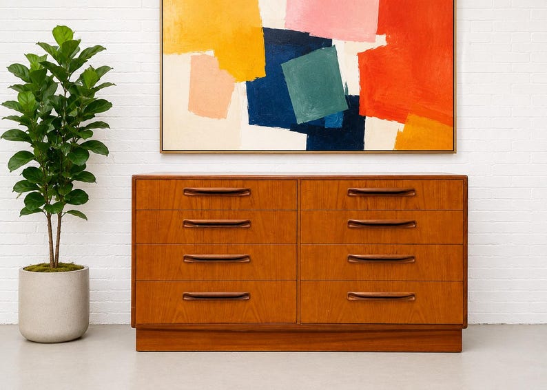 May include: A mid-century modern wooden dresser with eight drawers and dark brown handles. The dresser is made of light brown wood and sits on a low base. Above the dresser is an abstract painting with yellow, pink, blue, and red colors.