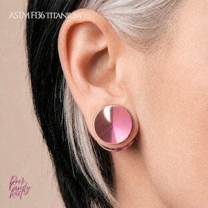 May include: A circular ear plug with a polished metallic pink finish inserted into an earlobe. The text ASTM F136 TITANIUM is visible in the upper left corner, and the text Rock Candy Riot is visible in the lower left corner of the image.