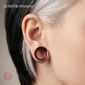 May include: A deep burgundy titanium ear tunnel gauge with a smooth, circular profile. The jewelry is made of ASTM F136 titanium and features a polished finish. The text ASTM F136 TITANIUM is visible in the upper left corner of the image.